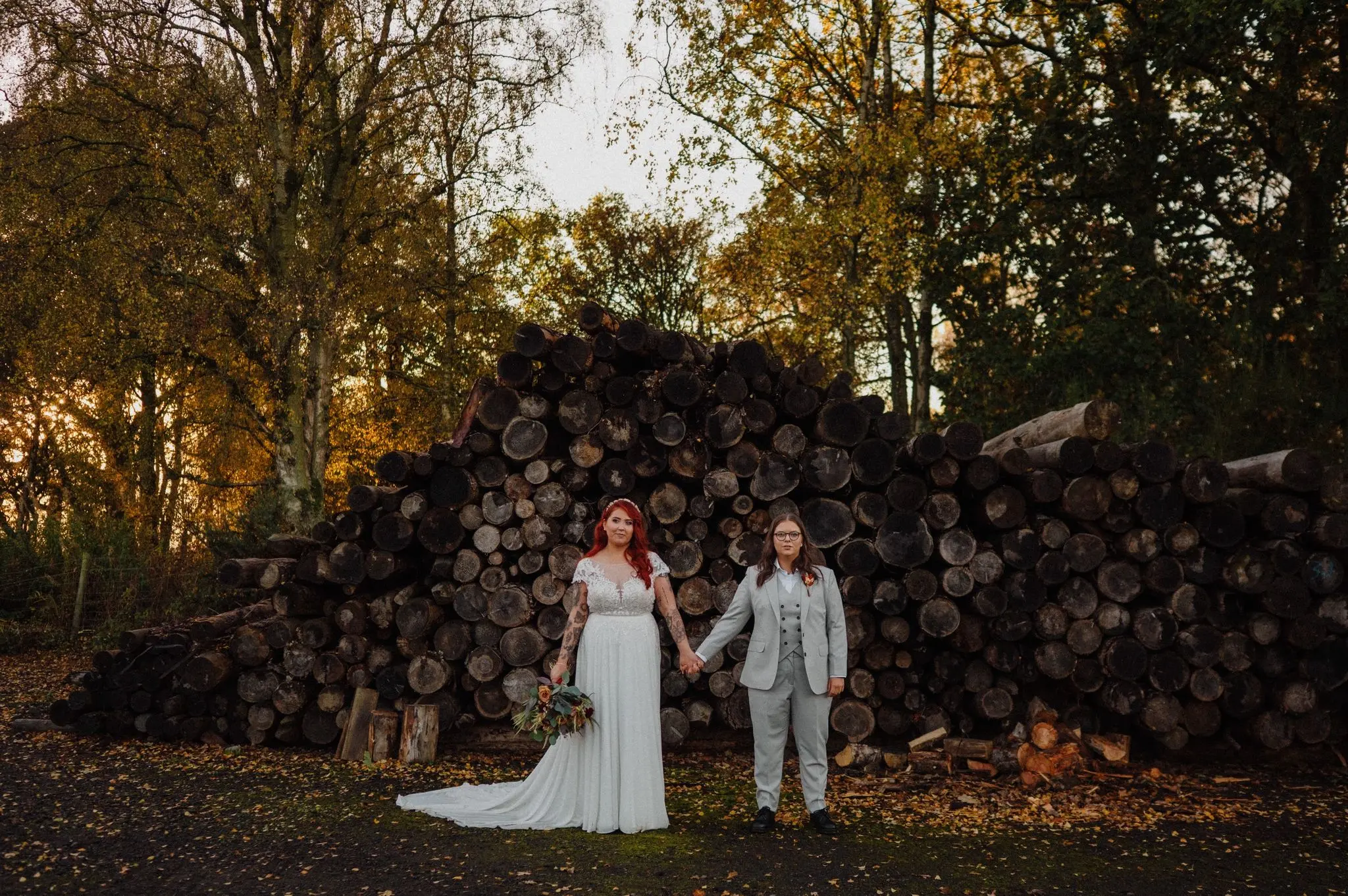 Autumn wedding couple beside stacked woodland